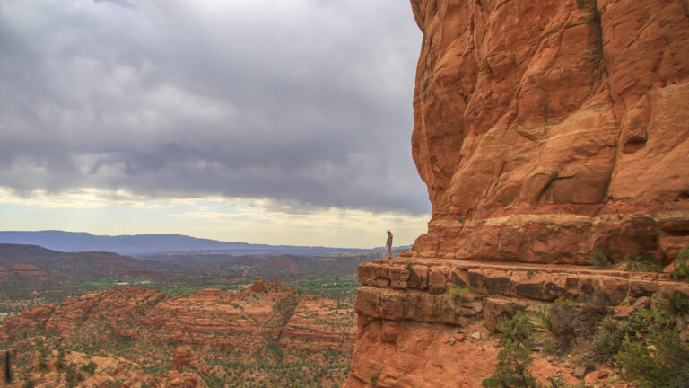 vecteezy_woman-standing-on-a-cliff-next-to-red-rocks_3054816